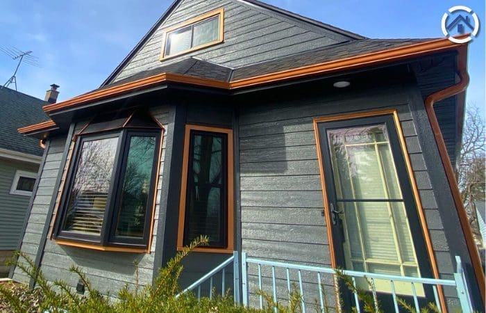 House exterior with LP siding in a dark gray color, accented by black-framed windows and orange trim, under a clear sky.