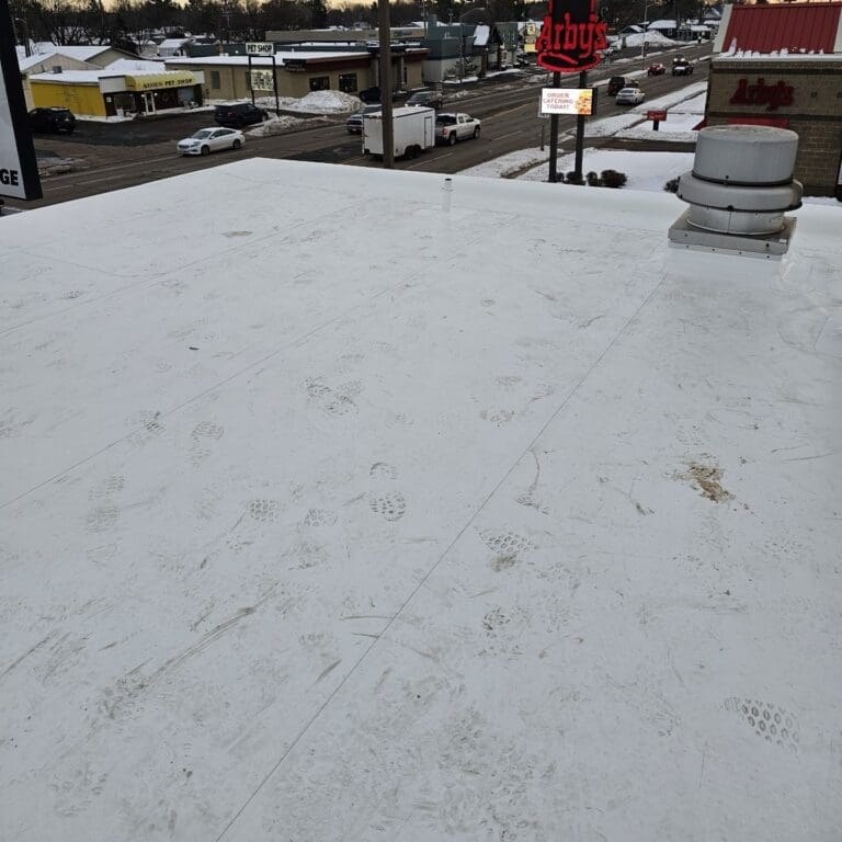 Finished white PVC flat roof at Take 5 Oil Change in Wisconsin Rapids with rooftop vent and surrounding commercial area visible