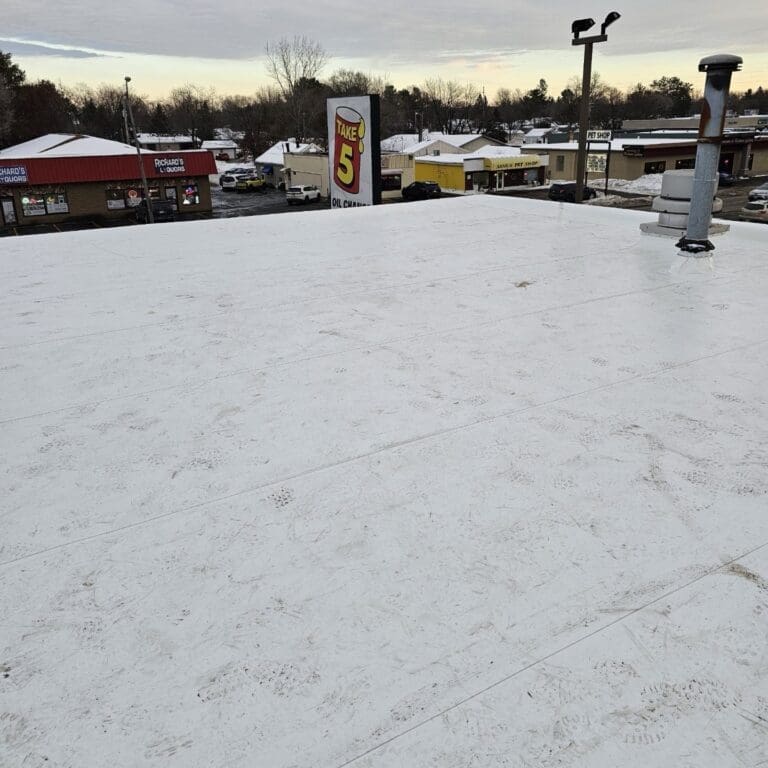 Wide view of newly installed white PVC roofing system at Take 5 Wisconsin Rapids with rooftop vents and surrounding businesses in background