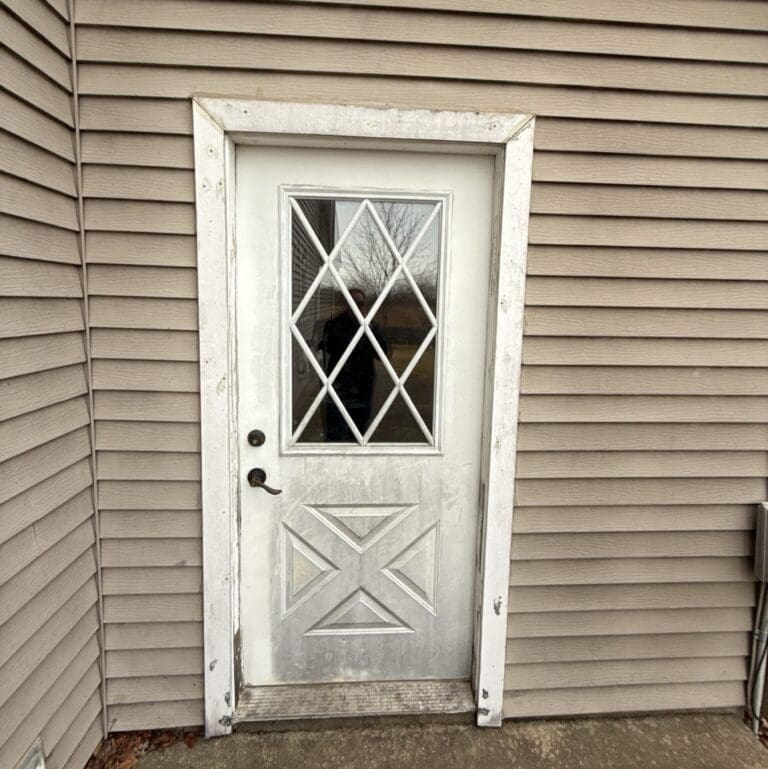 Close-up of aged door and surrounding trim showing peeling finish, wear, and deteriorating exterior materials