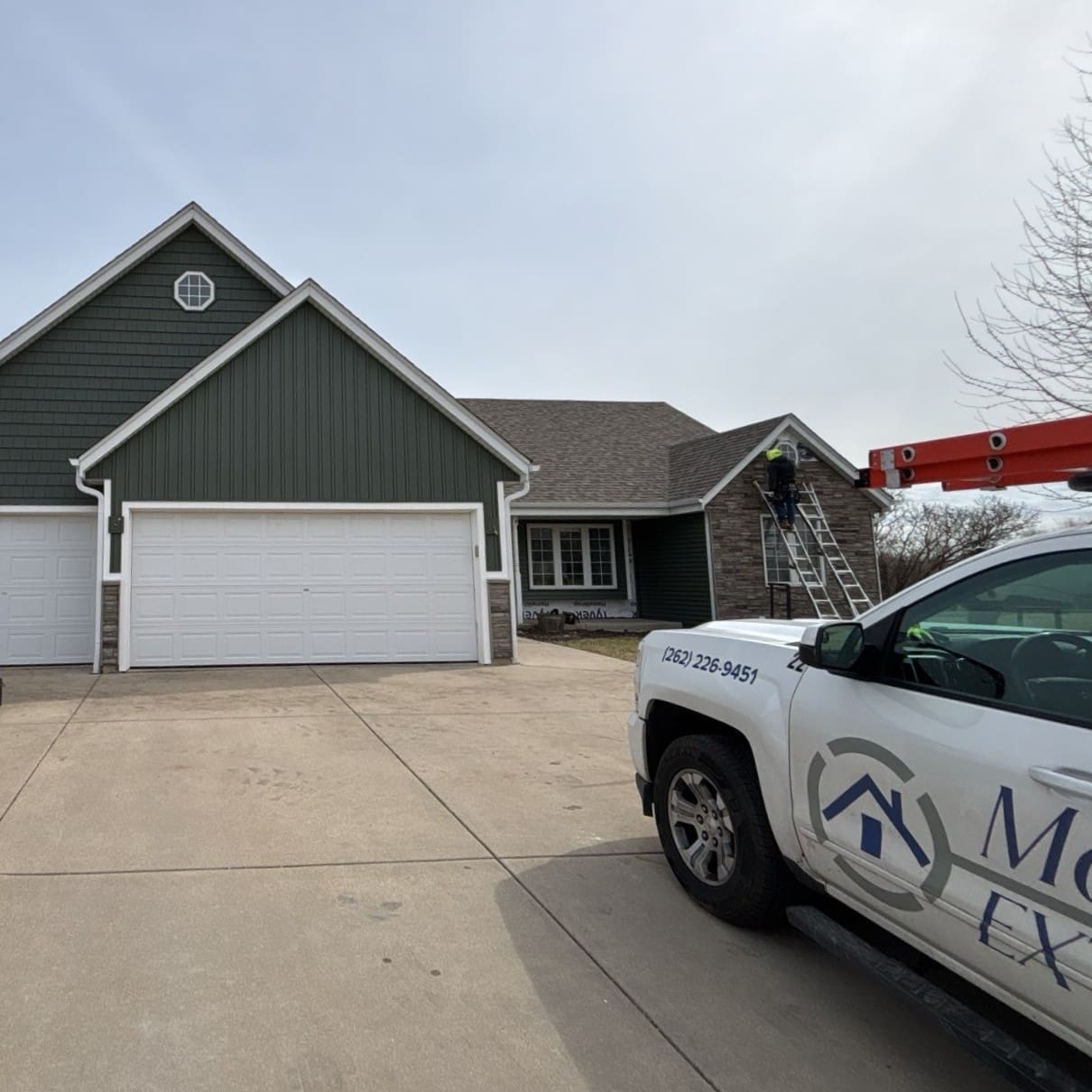 Modern Exterior installer on ladder finishing stone veneer accent on front of home with new siding and trim nearly complete
