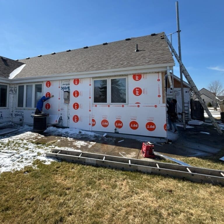 Crew installing exterior foam insulation boards over house wrap as part of siding preparation during renovation