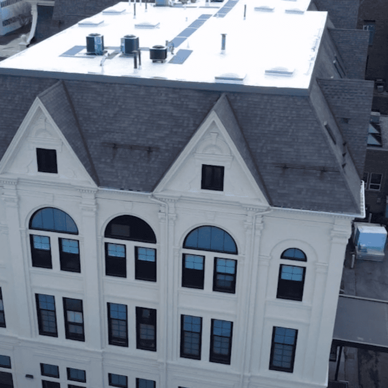 Side aerial view of the existing steep-slope shingle roof adjoining a flat roof before commercial roof replacement in Milwaukee.