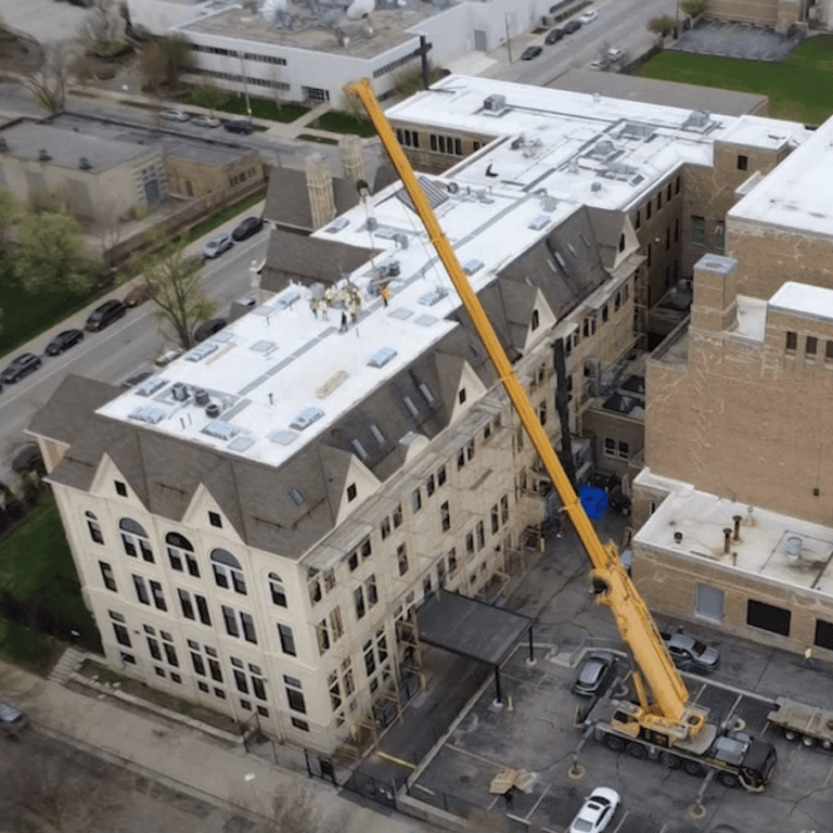 Crane loading roofing materials onto a large commercial building during a roof replacement project in Milwaukee.