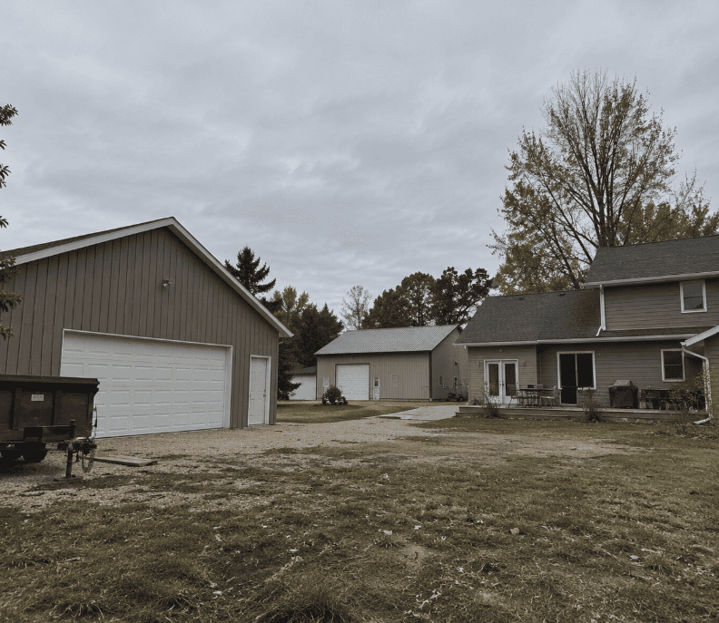 Rural property with a sided home, detached garage, workshop, and outbuildings featuring coordinated neutral exteriors.